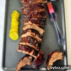 Fall-Off-The-Bone Oven Baby Back Ribs 13 oven baked ribs on a sheet pan with BBQ sauce and pickles