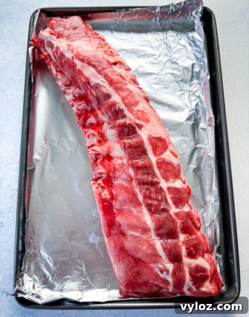 Fall-Off-The-Bone Oven Baby Back Ribs 3 raw ribs on a sheet pan with foil