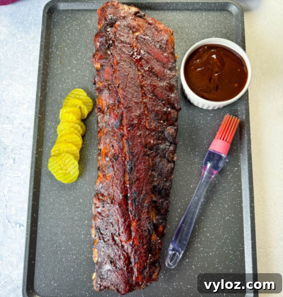 Fall-Off-The-Bone Oven Baby Back Ribs 10 oven baked ribs on a sheet pan with BBQ sauce and pickles