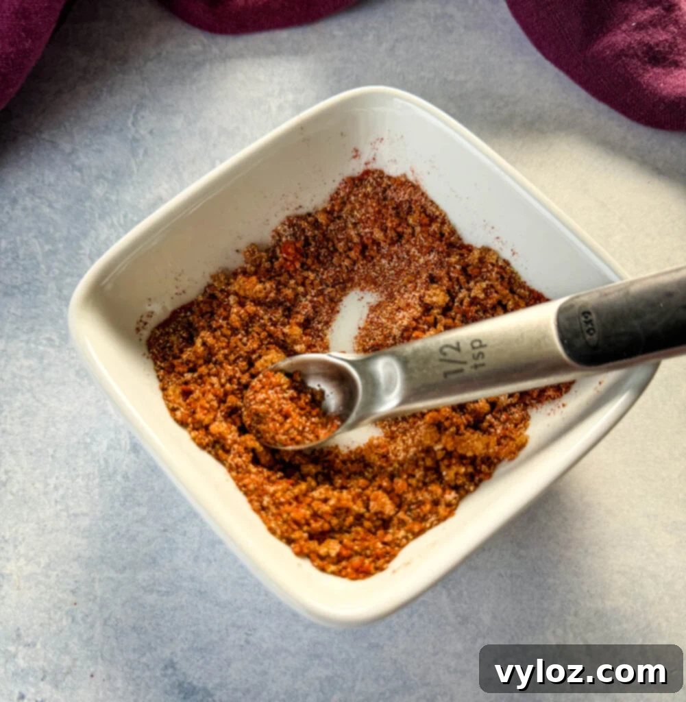 Assorted spices for rib dry rub in a white bowl with a spoon, ready to be mixed