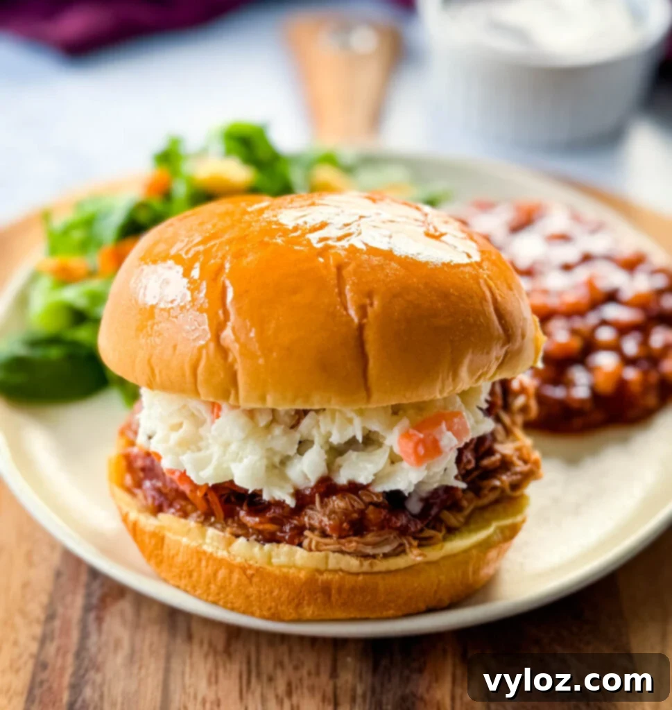 slow cooker Crockpot pulled chicken sandwich with BBQ sauce and coleslaw on a plate with baked beans
