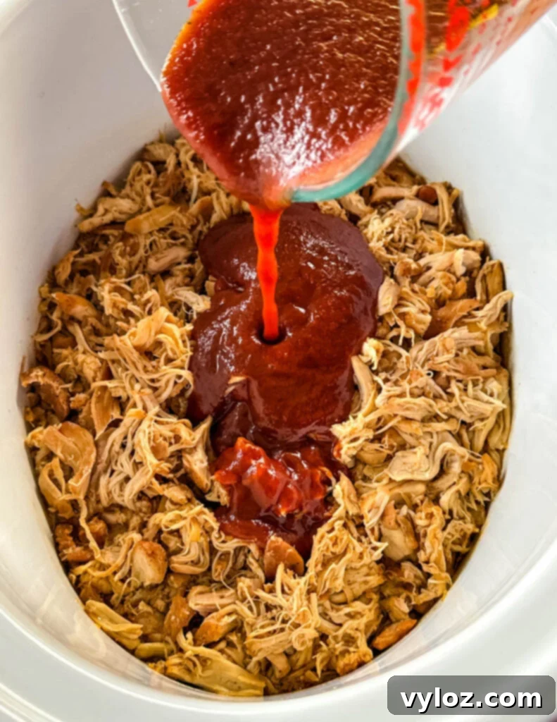 BBQ sauce drizzled over pulled chicken in a white Crockpot slow cooker