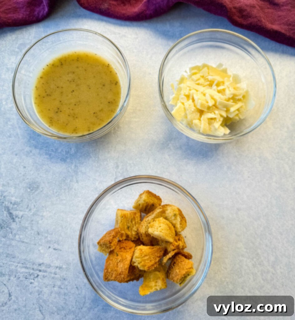 Caesar salad dressing, grated Parmesan cheese, and croutons in separate glass bowls
