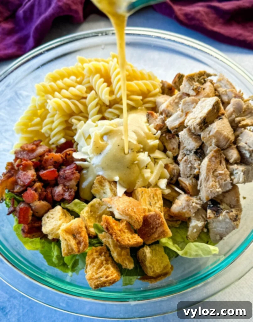 salad dressing drizzled over Chicken Caesar Pasta Salad with bacon and croutons in a glass bowl