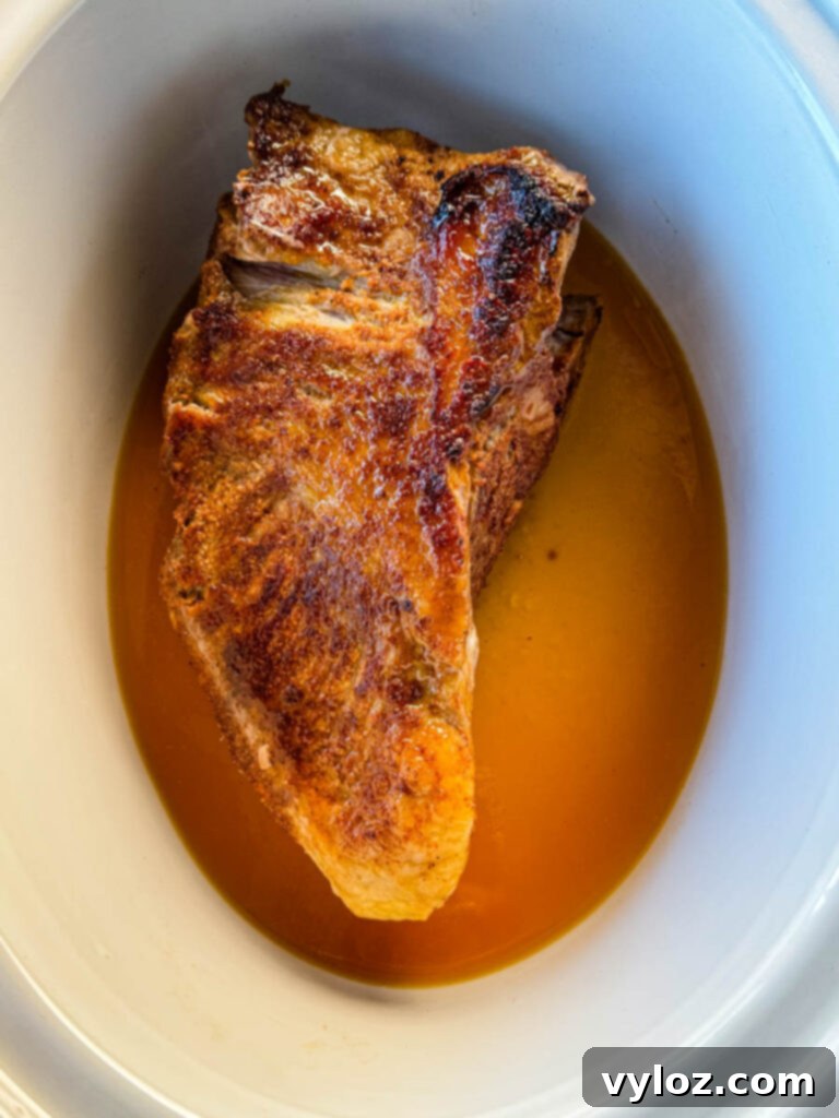 seared brisket and broth in a white Crockpot slow cooker