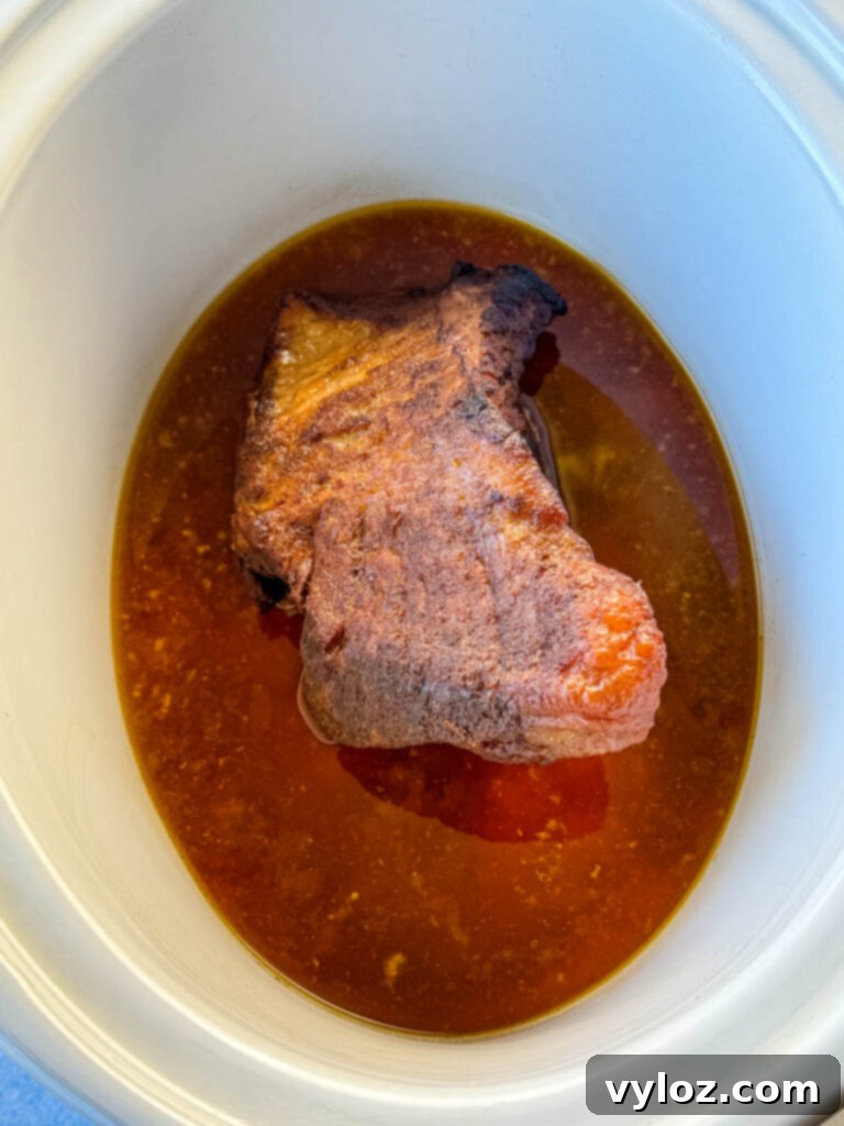 brisket in a white Crockpot slow cooker with broth