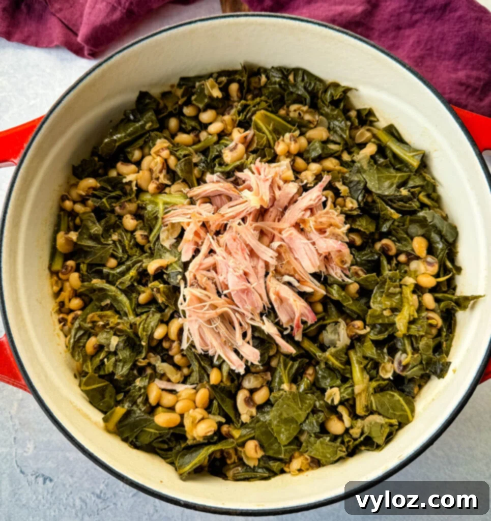 A close-up of a flavorful blend of collard greens, black-eyed peas, and smoked turkey, served in a red Dutch oven with a wooden spoon, highlighting the texture and rich broth.