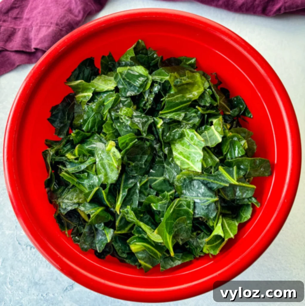 A vibrant red bowl overflowing with freshly washed and prepped collard greens, ready for cooking.