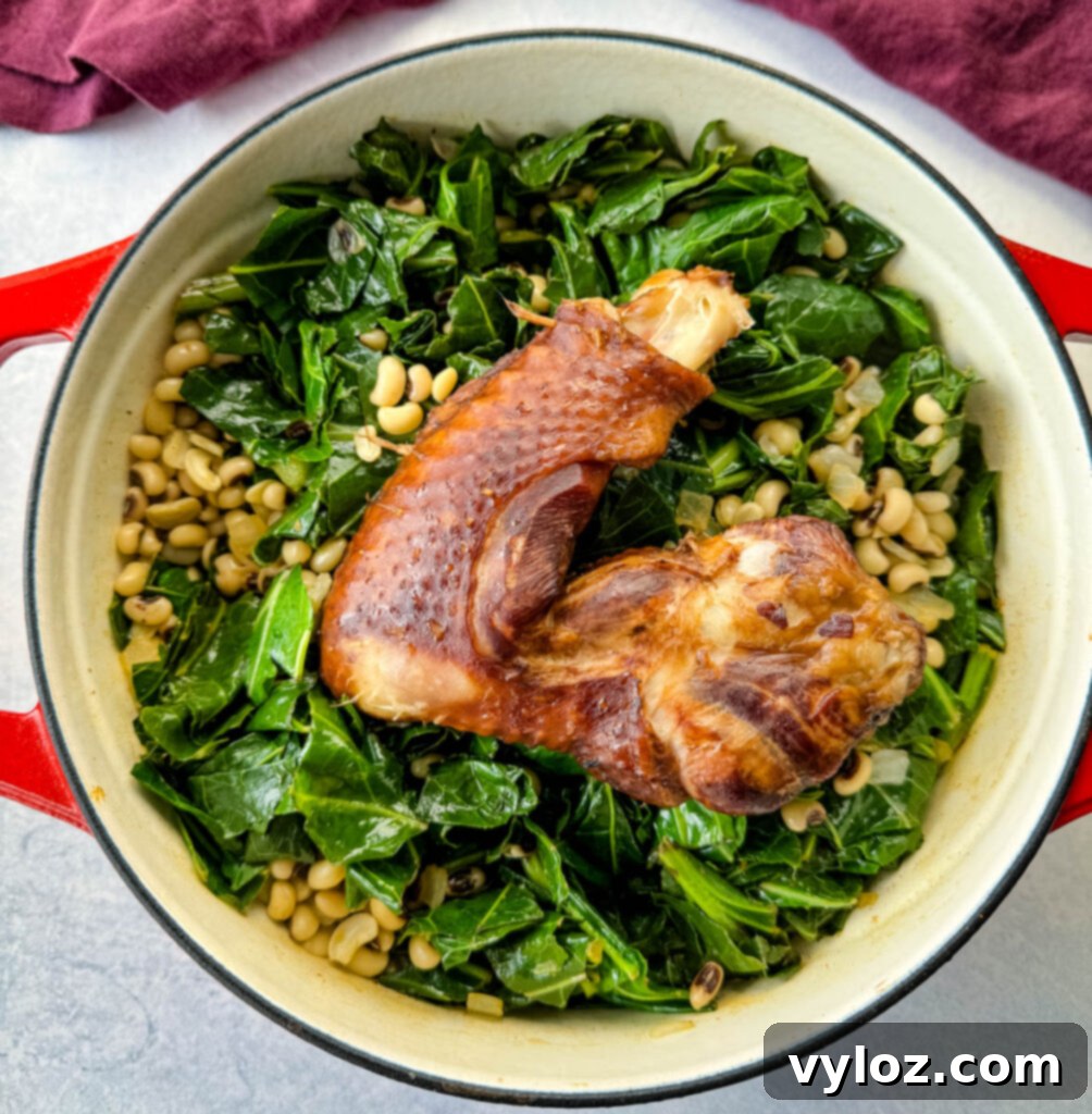 Hearty collard greens and black-eyed peas with tender smoked turkey in a red Dutch oven, a wooden spoon resting inside, signifying a completed and comforting meal.