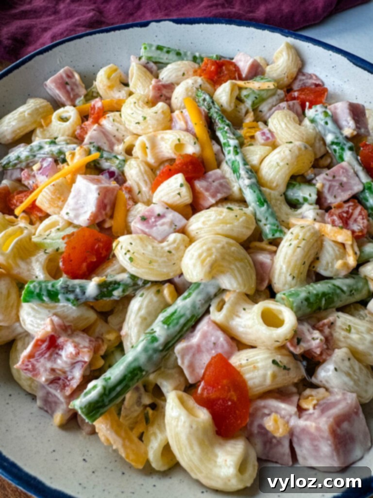 Classic Ham Pasta Salad 12 ham pasta salad with cheese, asparagus and tomatoes in a white bowl