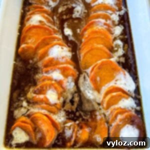 candied sweet potatoes with marshmallows in a baking dish drizzled with glaze in a wooden spoon