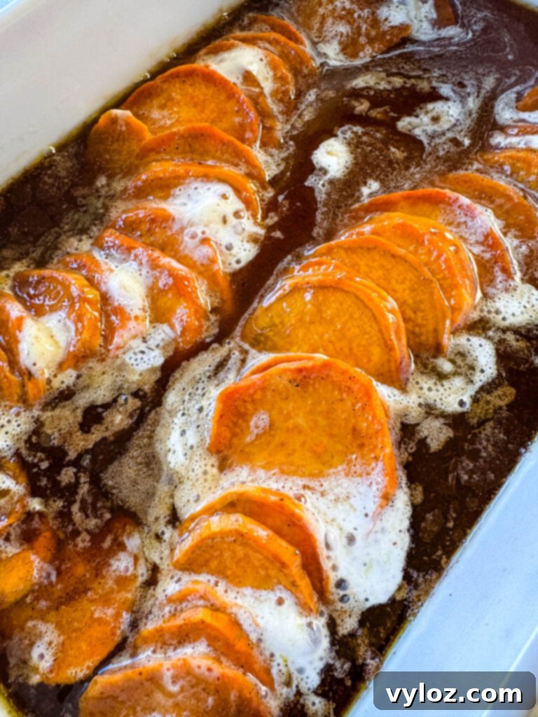 Serving of candied sweet potatoes with marshmallows in a wooden spoon, taken from a larger baking dish.