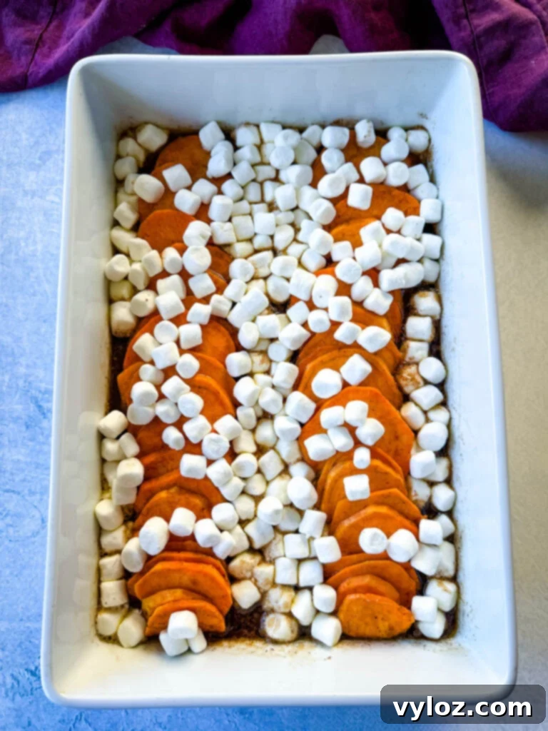 Sliced sweet potatoes generously topped with marshmallows and a glistening brown sugar cinnamon glaze in a white baking dish, ready for the final bake.