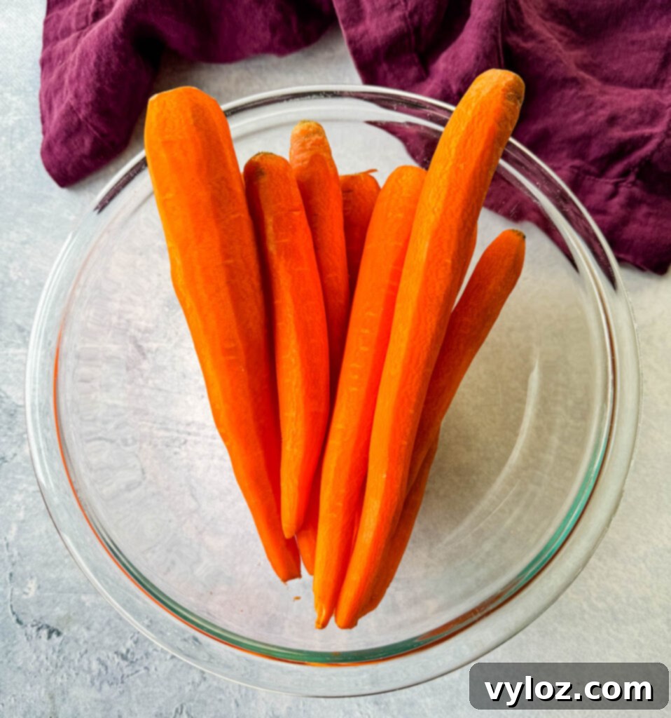 Sweet Glazed Carrots 4 Fresh, raw whole carrots in a clear glass bowl, ready for preparation.
