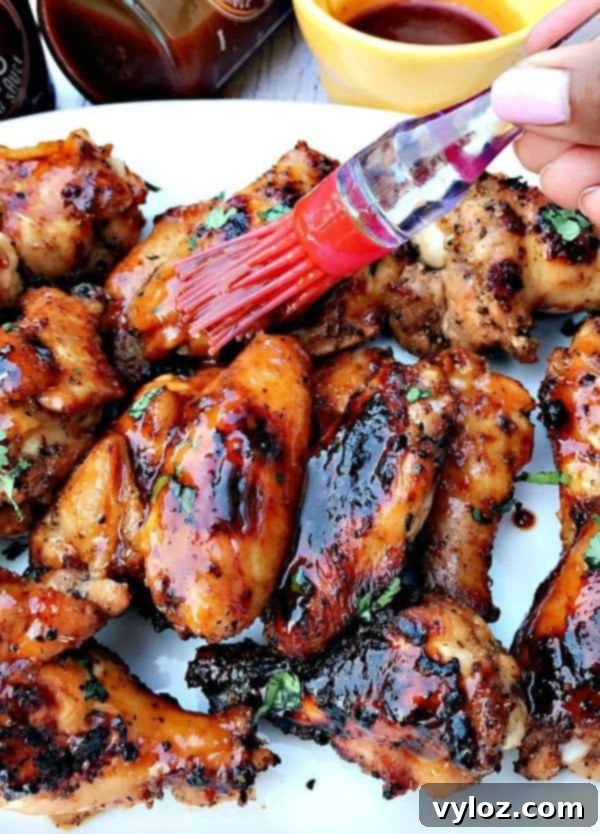 Charred BBQ Ranch Chicken Wings 5 A person applying BBQ sauce to grilled chicken wings with a brush.