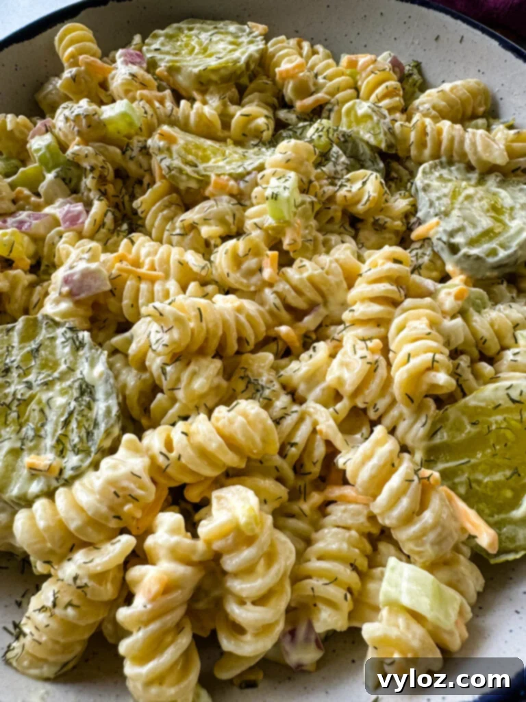 Zingy Dill Pasta Salad 11 A pristine white bowl filled with creamy dill pickle pasta salad, presented on a rustic wooden surface for an appetizing display.
