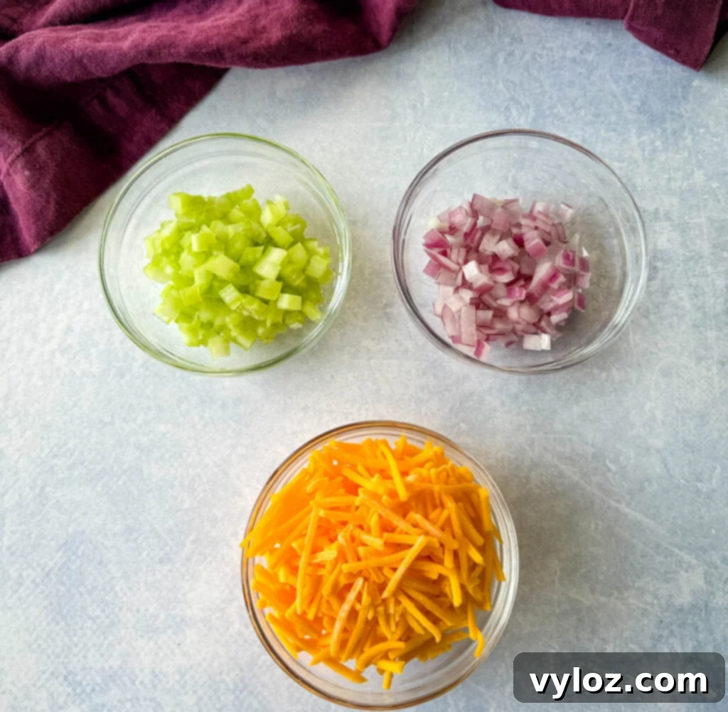 Zingy Dill Pasta Salad 3 Bowls of grated cheddar cheese, finely diced onions, and crisp diced celery, essential components for a flavorful pasta salad.