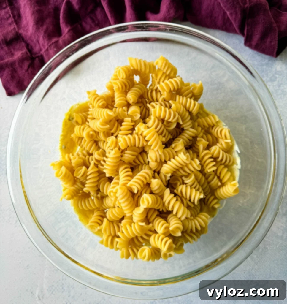 Zingy Dill Pasta Salad 6 A clear glass bowl filled with perfectly cooked and cooled rotini pasta, ready to be mixed into a delicious salad.