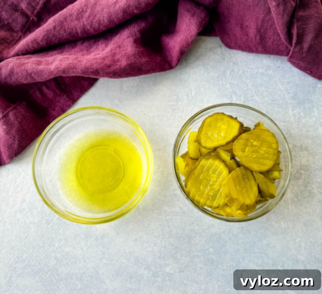 Zingy Dill Pasta Salad 7 Separate glass bowls containing a generous amount of chopped pickles and a portion of pickle juice, highlighting key salad ingredients.