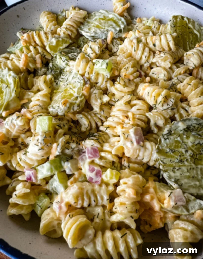 Zingy Dill Pasta Salad 10 A pristine white bowl filled with creamy dill pickle pasta salad, presented on a rustic wooden surface for an appetizing display.