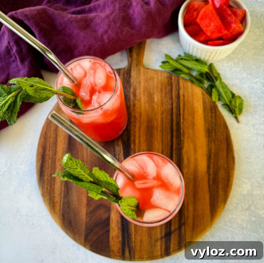 A glass of watermelon water, elegantly garnished with fresh mint leaves and ice, against a bright background.