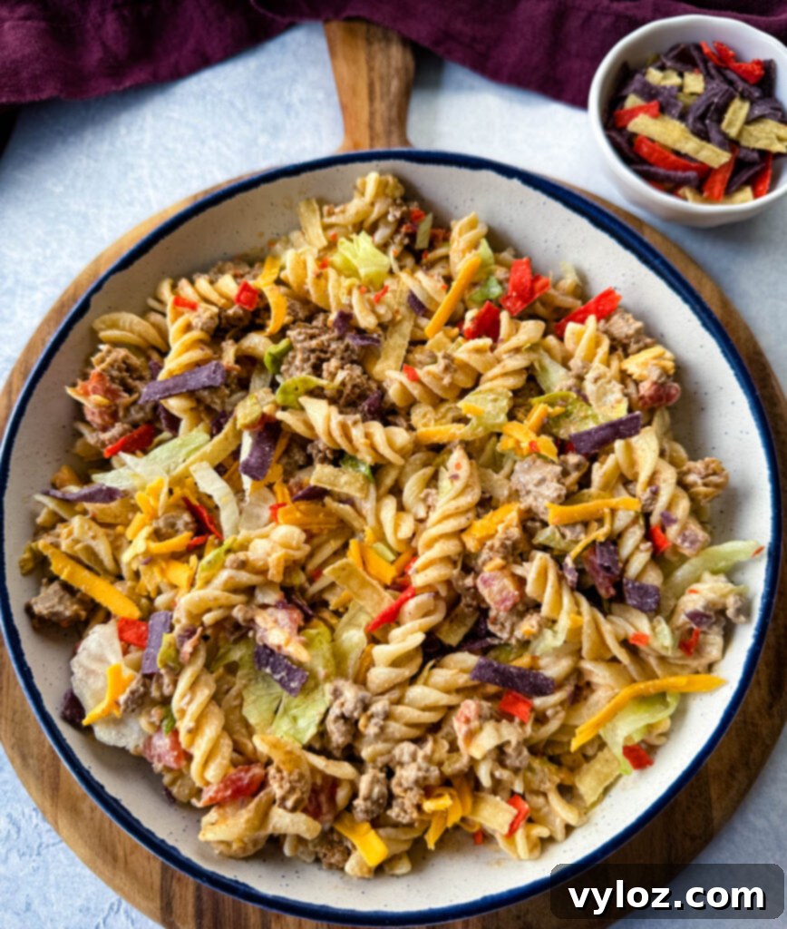 Taco pasta salad with chips, cheese, and lettuce, in a white bowl