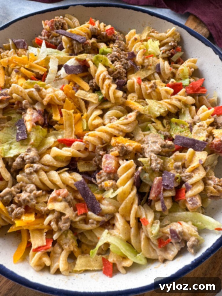 Taco pasta salad with chips, cheese, and lettuce, in a white bowl