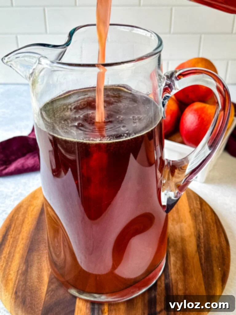 Peach simple syrup being poured into a pitcher of iced tea