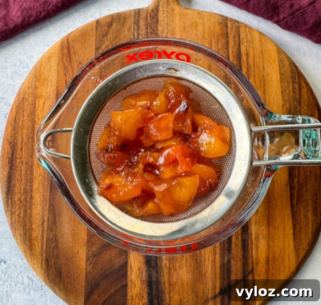 Pureed peaches and simple syrup being strained through a mesh strainer