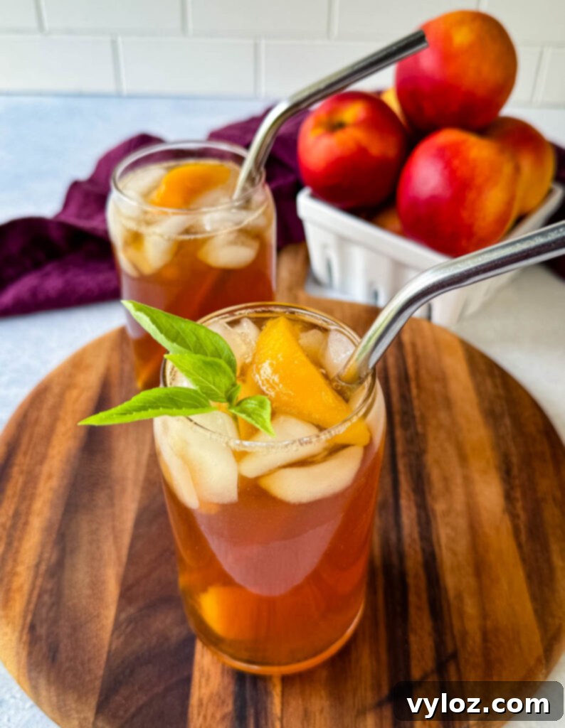 Homemade peach tea in a glass with basil, peaches, and a straw, garnished and ready to serve