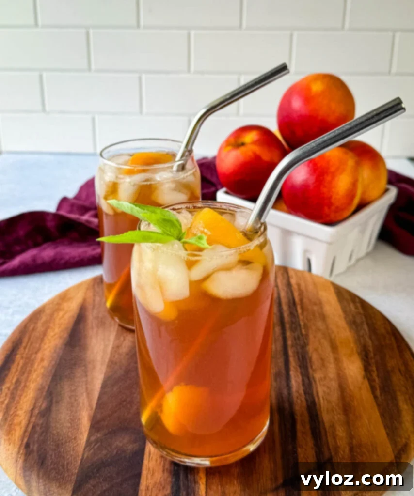 Homemade peach tea in a glass with basil, peaches, and a straw, a perfect refreshing beverage