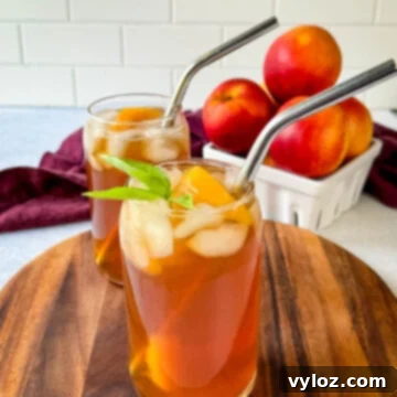 Homemade peach tea in a glass with basil, peaches, and a straw