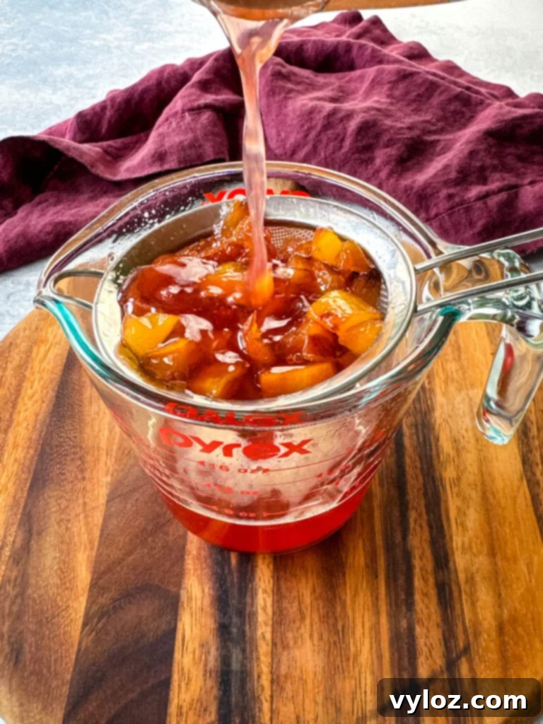 Pureed peaches and simple syrup being strained through a mesh strainer into a glass bowl