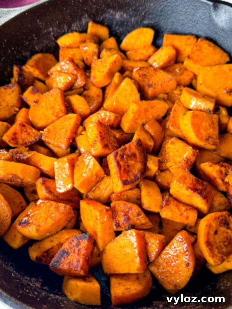A vibrant display of fried sweet potatoes in a cast iron skillet, garnished with fresh herbs, showcasing their golden-brown perfection.