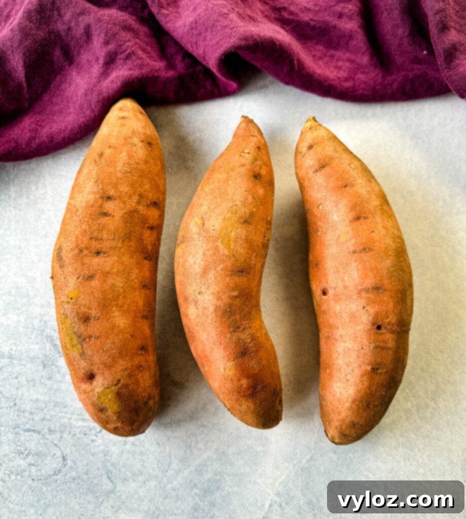 Raw, unpeeled sweet potatoes lying on a flat wooden surface, ready for preparation.