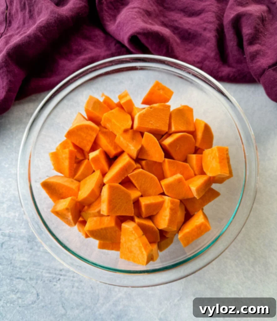 Diced sweet potatoes seasoned with spices in a clear glass bowl, prepped for frying.