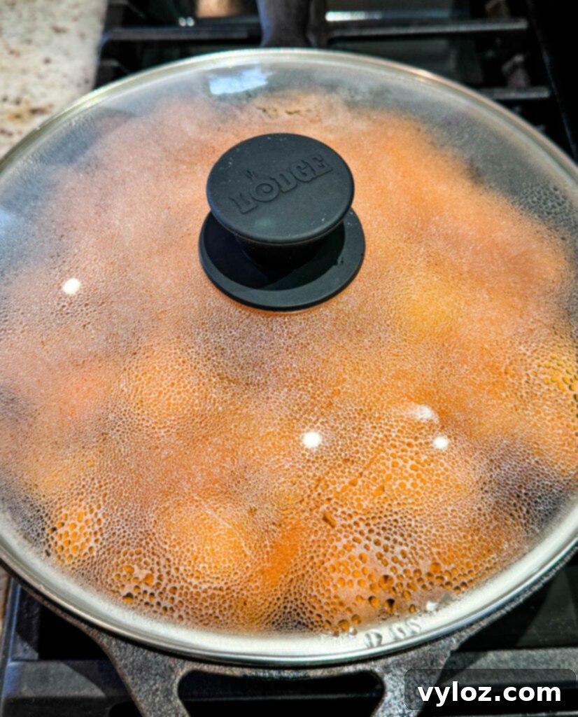 Cast iron skillet filled with sweet potato slices, covered with a lid to steam and tenderize.