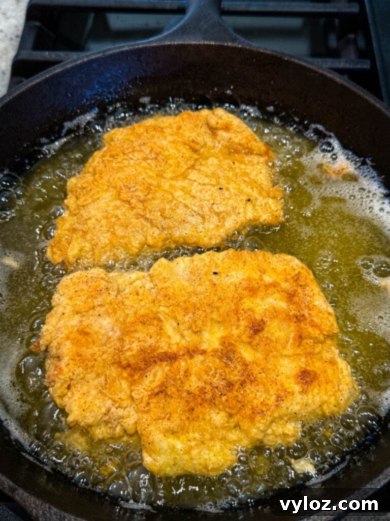 Golden brown chicken fried chicken pieces sizzling in a cast iron skillet with hot oil.