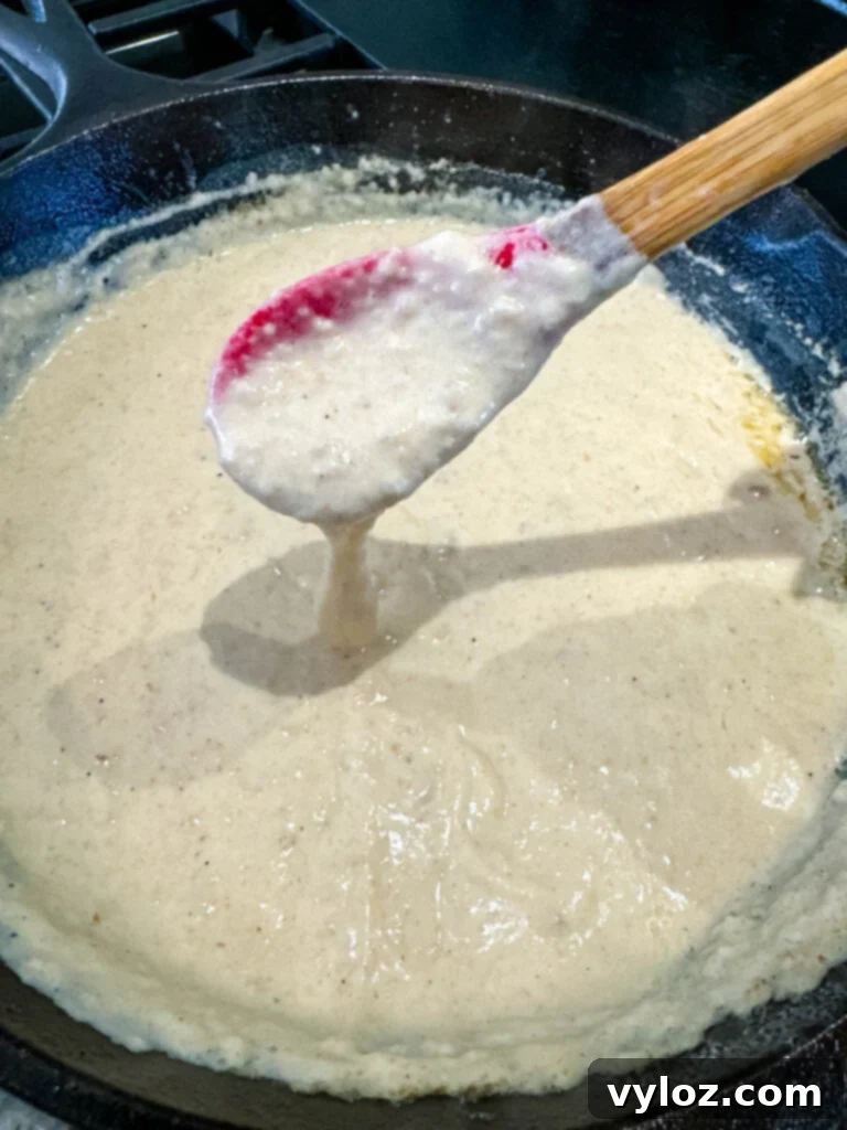 A spoon lifting a creamy, rich spoonful of homemade country gravy from a cast iron skillet.