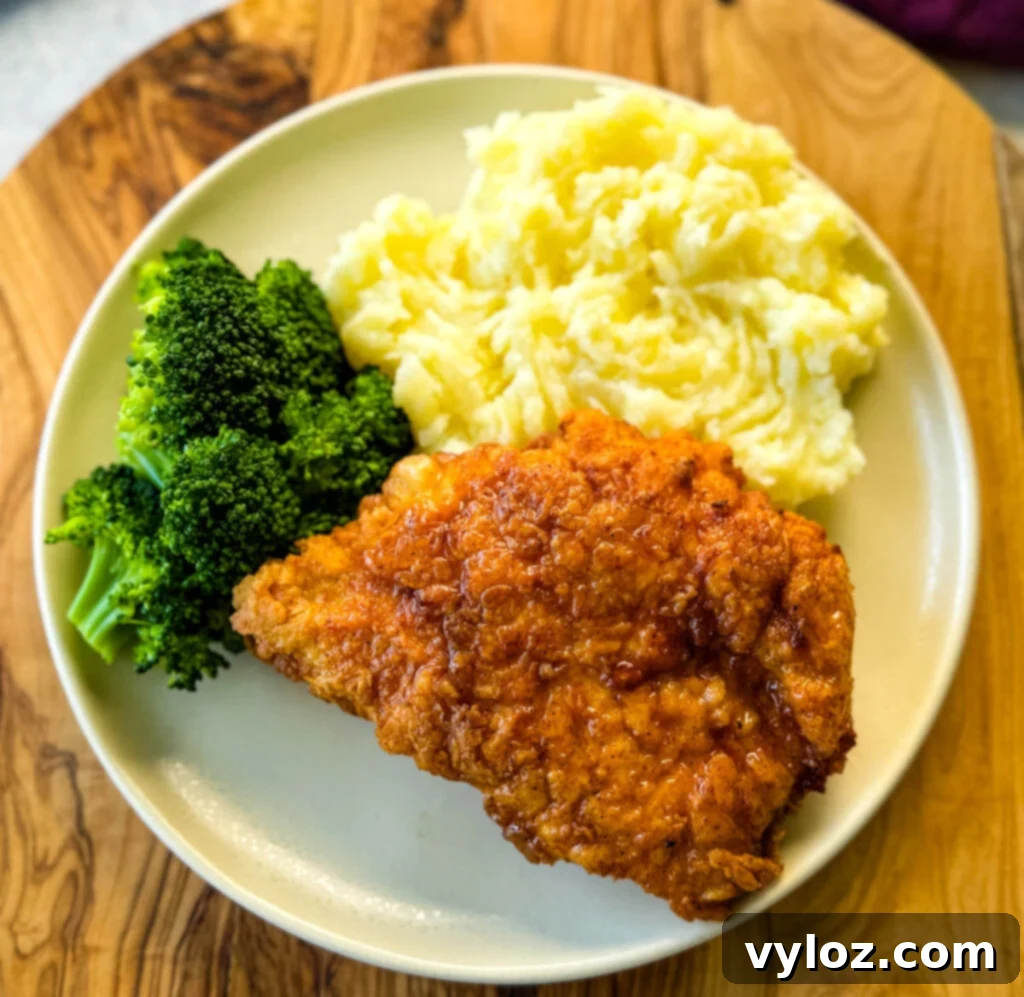A full plate of chicken fried chicken topped with gravy, served alongside creamy mashed potatoes and vibrant green broccoli.