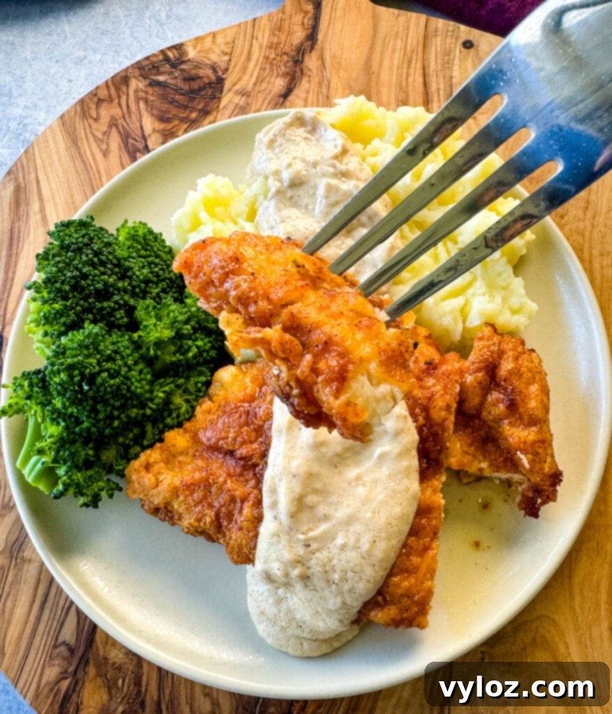 A fork holding a piece of crispy chicken fried chicken, generously drizzled with rich country gravy.
