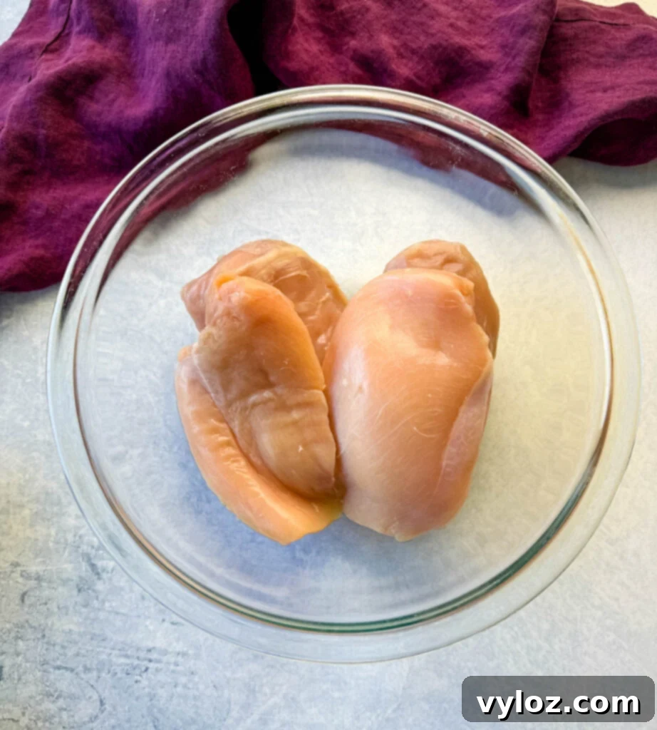 Raw, boneless, skinless chicken breasts in a clear glass bowl, ready for preparation.