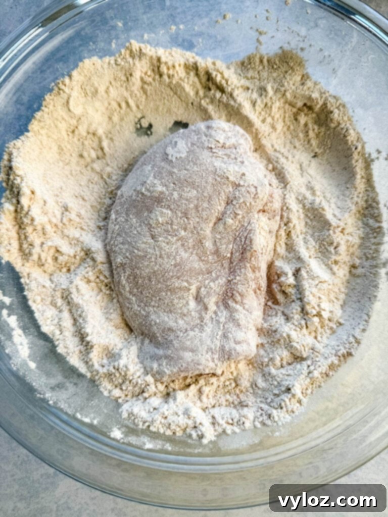 Raw chicken breast perfectly coated in seasoned flour in a glass bowl.