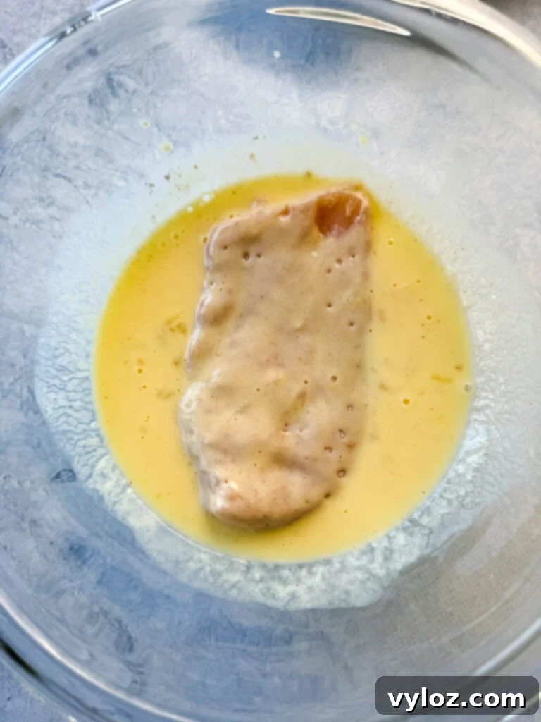 Raw chicken breasts coated in an egg and buttermilk mixture, ready for the second flour dredge.