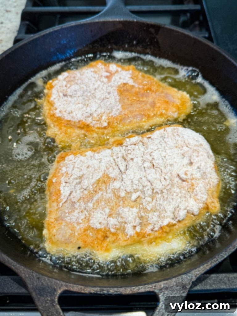 Uncooked, breaded chicken fried chicken in a cast iron skillet with hot oil, prepared for pan-frying.