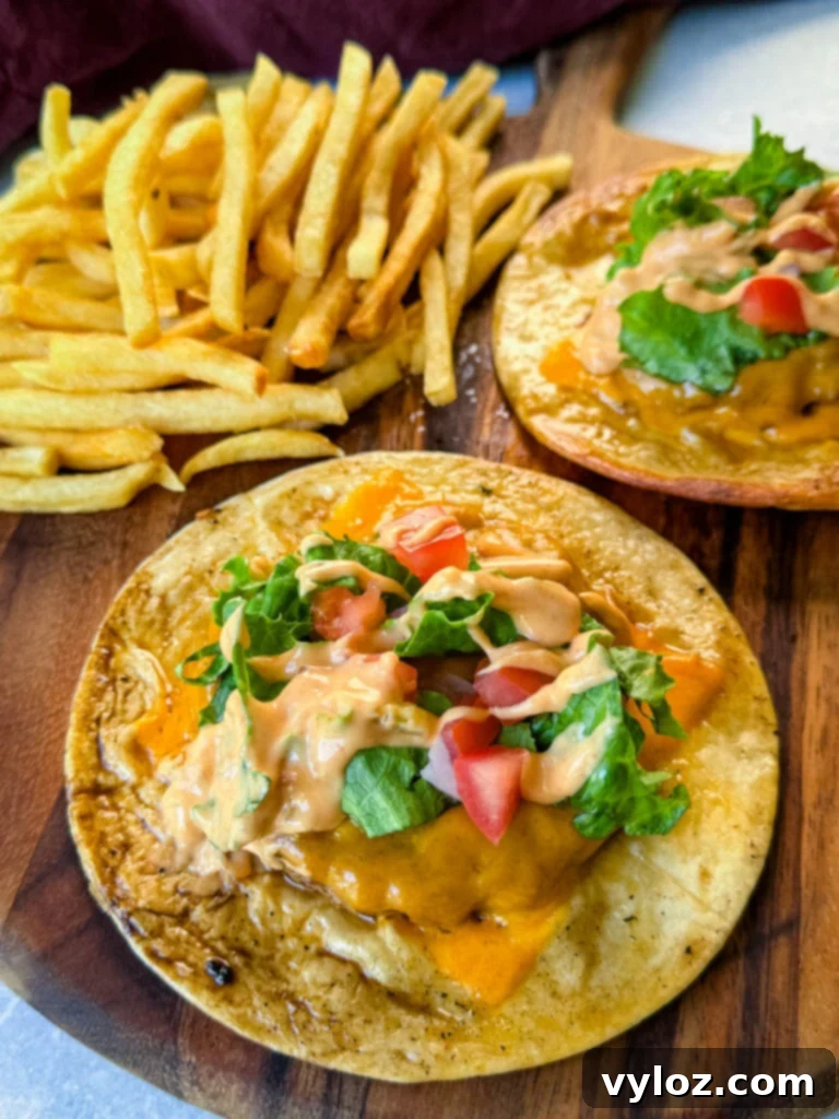 Cheesy Taco Burgers 2 cheeseburger tacos with tomatoes, lettuce, and burger sauce on a plate with fries