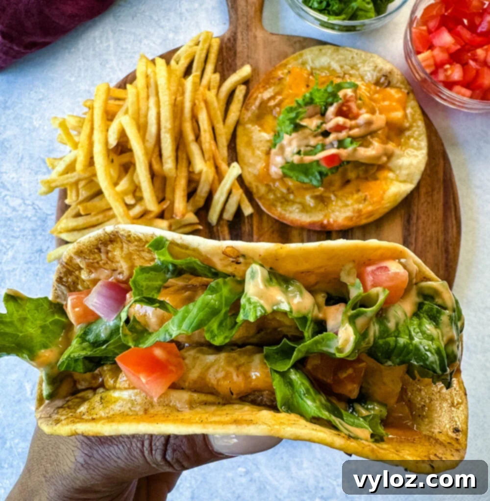 Cheesy Taco Burgers 11 person holding cheeseburger tacos with tomatoes, lettuce, and burger sauce over a plate with fries