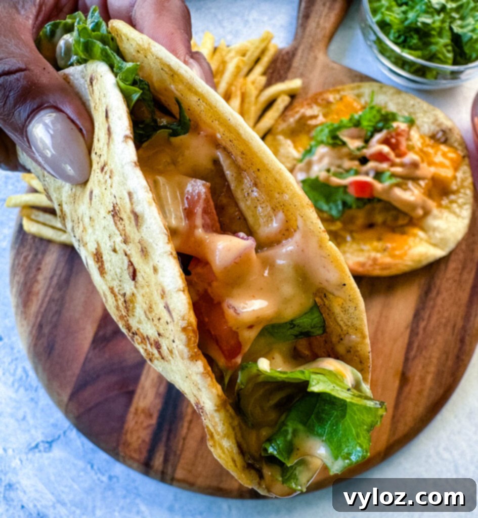 Cheesy Taco Burgers 13 person holding cheeseburger tacos with tomatoes, lettuce, and burger sauce over a plate with fries
