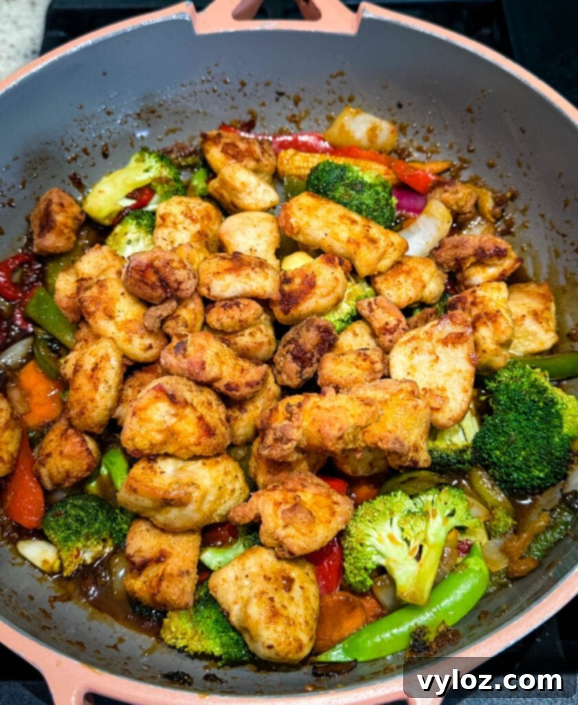 Cooked orange chicken and stir-fried vegetables generously coated in sauce within a large skillet.