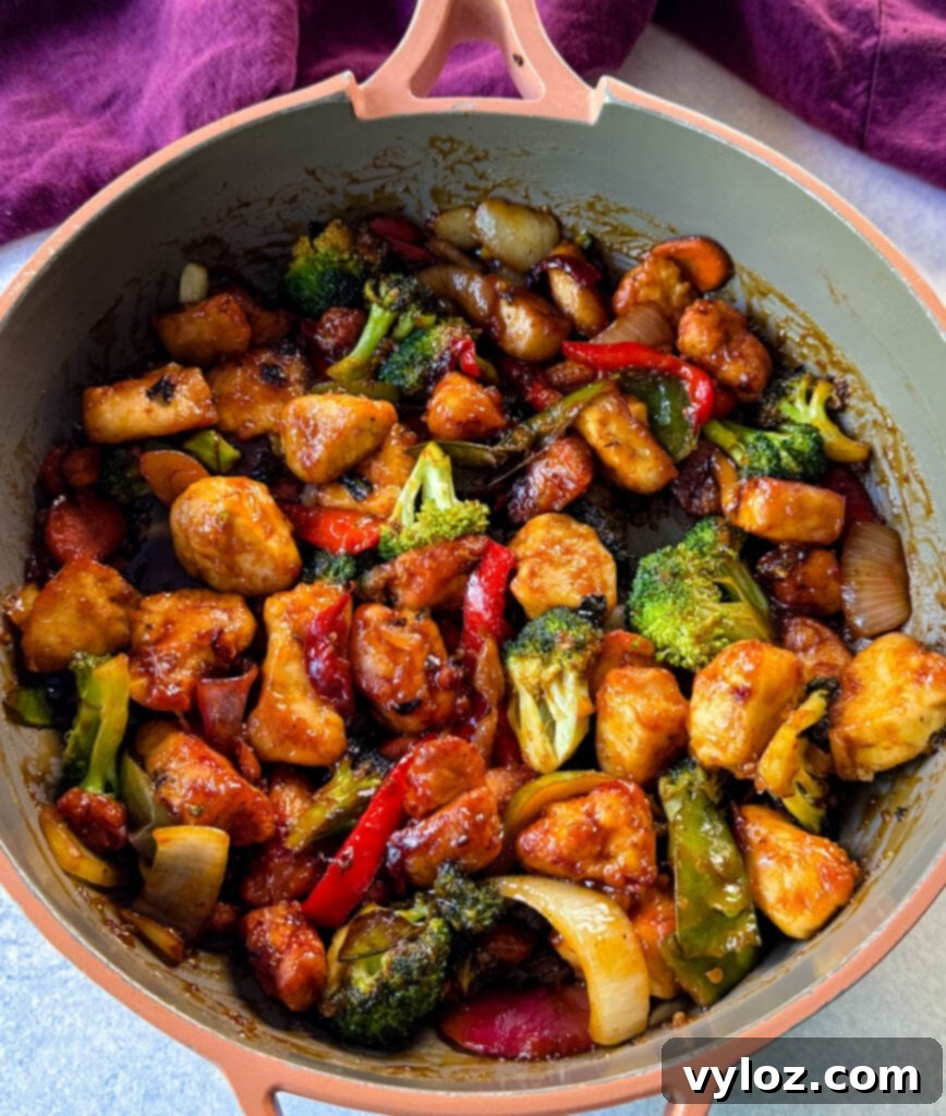 Orange chicken with stir-fried vegetables glistening in the sauce within a large skillet.